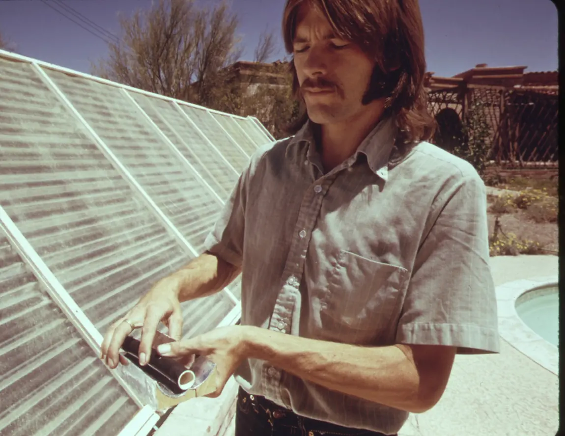 Archival colour photograph, 1974: a pool technician working on equipment at the edge of a backyard pool.